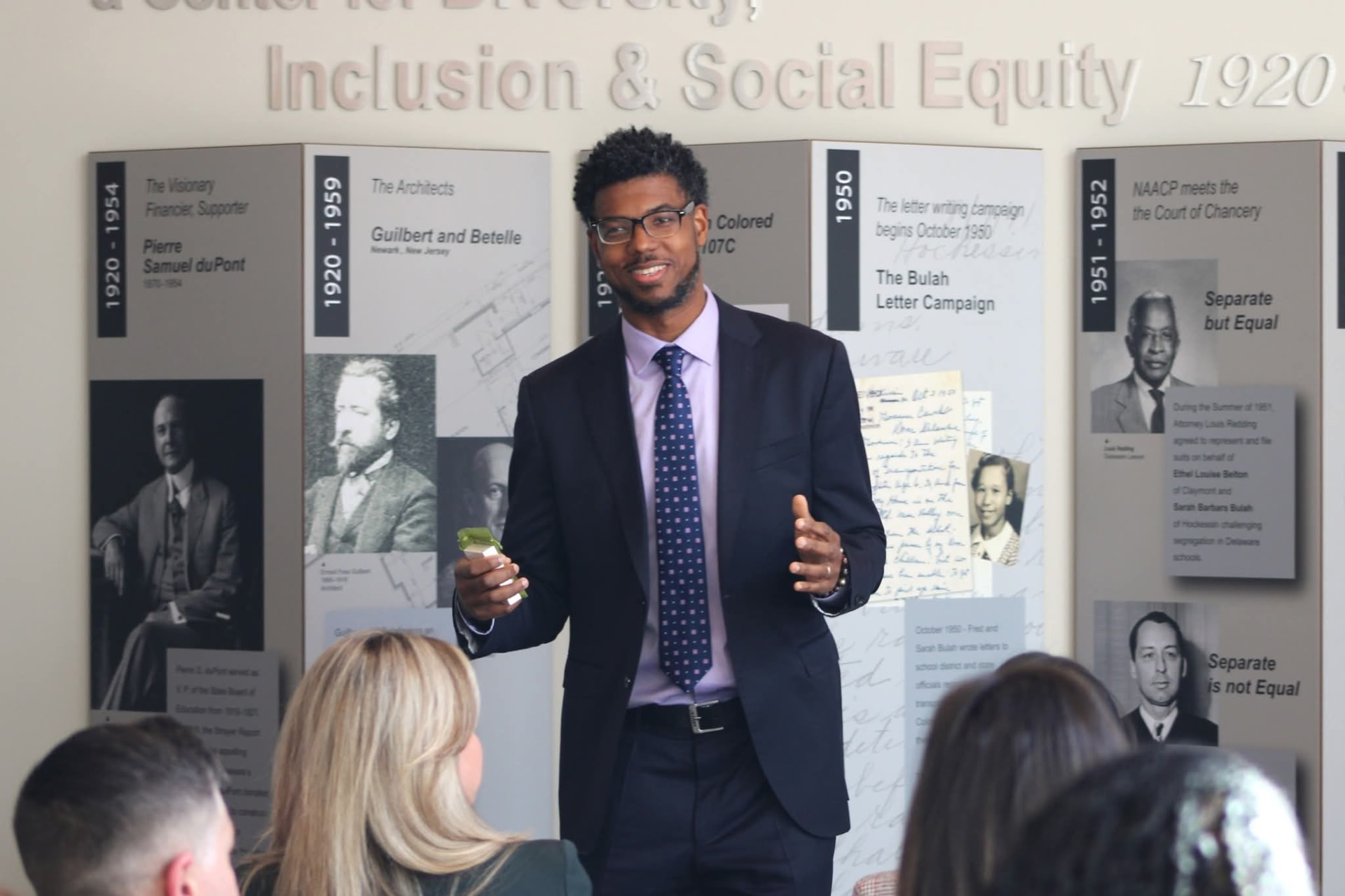 Atnre Alleyne speaking to a seated group in front of a civil rights history exhibit
